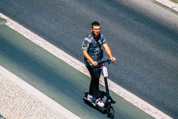 Lisbona Portogallo 25 luglio 2020 Veduta di persone non identificate che rotolano con uno scooter elettrico per le strade di Lisbona, che operano con una piccola utility motori a combustione interna e un ponte al centro - Foto, immagini