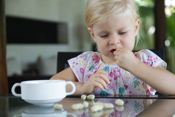 Pikkulapsi tyttö syö pähkinöitä kuori keittiön pöydälle - Valokuva, kuva