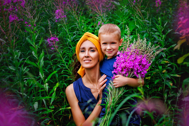 Мати в жовтому тюрбані з сином на полі. Жінка тримає букет рожевих квітів вузьколитої кипарис Іван-чаю і її сина. Вони щасливі. Вибіркове фокусування і тонування зображення. - Фото, зображення