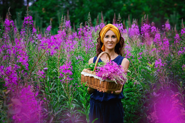 Een jong meisje verzamelt een boeket roze bloemen in een veld van smalle cipres Ivan thee. Een vrouw loopt en geniet van een bloeiend veld. Houdt een mand bloemen vast. - Foto, afbeelding