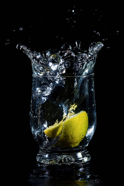 Salpicadura de agua en vidrio con limón en fondo negro aislado  - Foto, Imagen