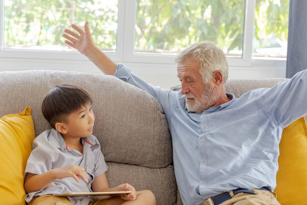 Nonno e nipotino carino giocare tablet PC touchscreen insieme sul divano nella loro casa - Foto, immagini
