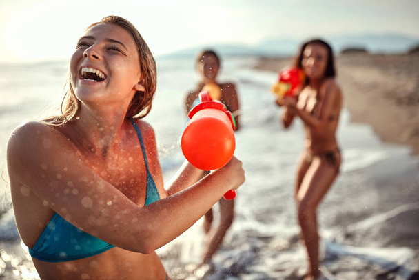 young blonde turned head away from two brunette friends shooting from water guns. friends having fun - 写真・画像