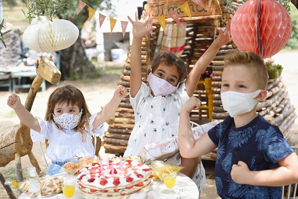 Tři malé děti slaví narozeniny s opatřeními na ochranu zdraví a maskou. - Fotografie, Obrázek