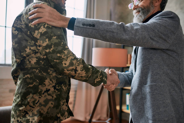 Caring hands. Cropped shot of mature psychologist smiling, shaking hands with middle aged military man after therapy session. Soldier suffering from depression, psychological trauma. PTSD concept - Photo, image