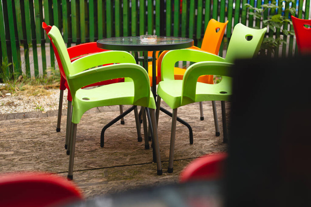 Prázdný stůl a židle na terase kavárny za oblačného a deštivého dne. Velmi živé barvy a barevný exteriér.  - Fotografie, Obrázek