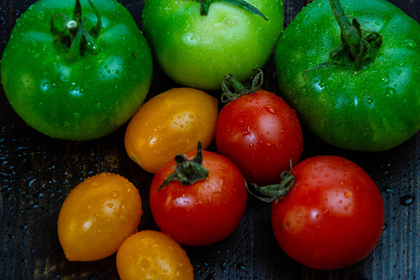 zátiší s čerstvými červenými, zelenými a žlutými rajčaty čerstvě sklizenými ze zahrady na dřevěném stole a kuchyňským nožem - Fotografie, Obrázek