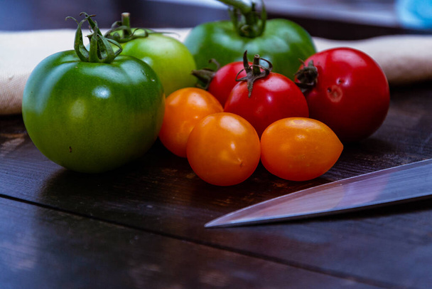 натюрморт зі свіжими червоними, зеленими та жовтими помідорами, що свіжо підібрані з саду на дерев'яному столі та кухонному ножі
 - Фото, зображення