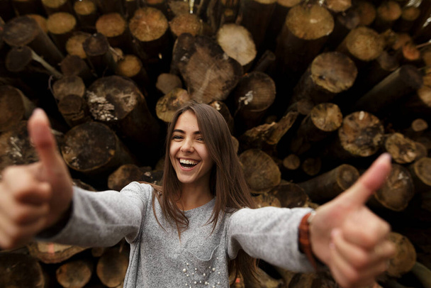 Image of satisfied happy smiling young brunette woman posing isolated over wooden wall background showing thumbs up with two hands. Excellent purchase! - Photo, Image