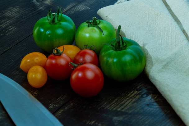 stilleven met verse rode, groene en gele tomaten vers geplukt uit de tuin op de houten tafel en keukenmes - Foto, afbeelding