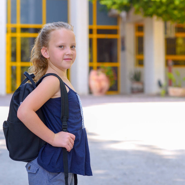 Portret szczęśliwego uśmiechniętego dzieciaka z powrotem do szkoły. Mała piegowata dziewczynka z torbą chodzi do szkoły podstawowej. Dziecko z podstawówki. Uczeń iść studiować z plecakiem. - Zdjęcie, obraz