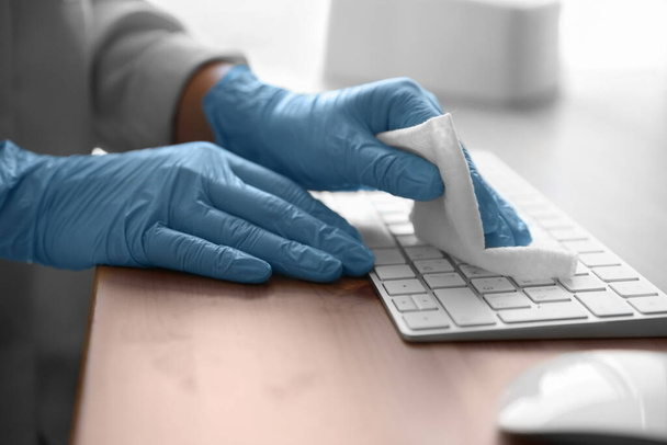 Woman in latex gloves cleaning computer keyboard with wet wipe at table, closeup - Photo, Image