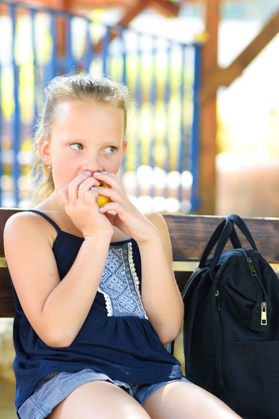 Little girl is eating an apple. Healthy nutrition. Pretty child eating an apple at park , nature outdoors. Teenager pupil enjoying healthy lunch in schoolyard. - Foto, immagini