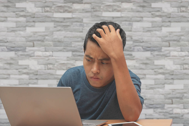 Hombre asiático con una camiseta casual. se estresa con el trabajo excesivo mirando un ordenador portátil, el trabajo desde el concepto de casa
. - Foto, Imagen