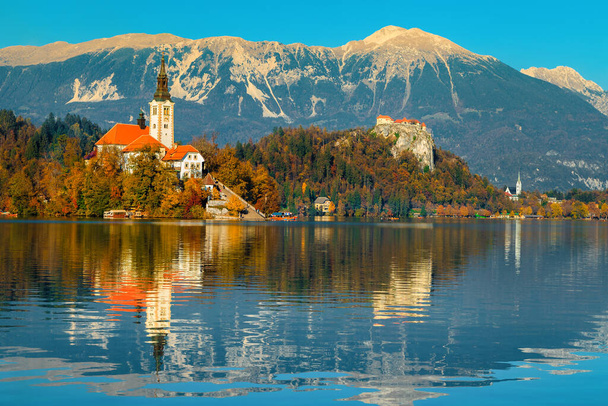 Herfst landschap met meer Bled. Leuke bedevaartskerk aan de oever van het meer en spectaculaire vesting op de kliffen op de achtergrond, Bled, Slovenië, Europa - Foto, afbeelding