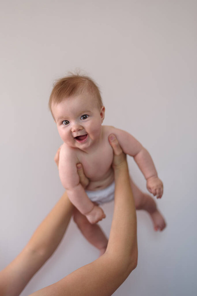 Mother holding baby girl 6 months aloft at home, low angle view - Foto, afbeelding