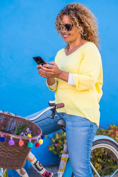 Portré vidám fiatal felnőtt nő használja a mobiltelefon, miközben ül egy vintage trendi kerékpár  - Fotó, kép