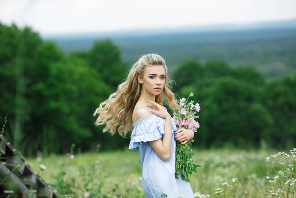 Letni portret pięknej dziewczyny z długimi blond włosami i pięknymi kwiatami w lecie. - Zdjęcie, obraz