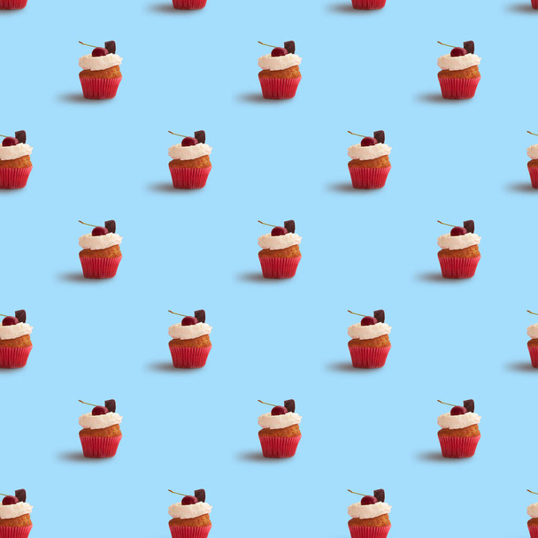 Tasty cupcake seamless pattern on blue background. Cupcakes decorated with cherry and chocolate - Fotografie, Obrázek