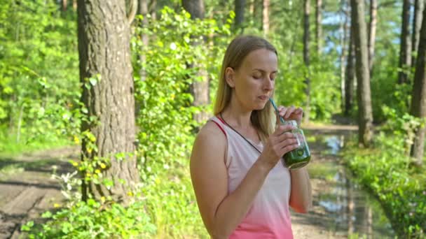 Sportos szőke nő a parkban turmixot iszik - Felvétel, videó