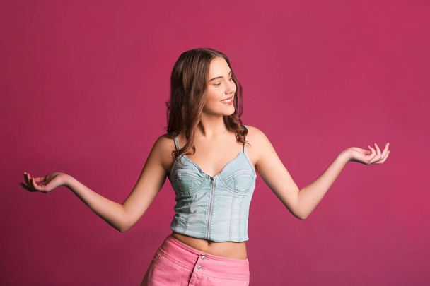 Laughing beautiful girl is pointing to product. Cheerful attractive young woman smiling and pointing away over pink background - Fotografie, Obrázek