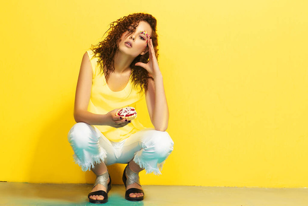Schöne junge kurzhaarige weibliche Modell mit Afro-Locken in gelb posiert auf gelbem Hintergrund. Nahaufnahme Porträt eines stylischen trendigen Teenagers vor gelber Wand. - Foto, Bild