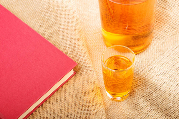 μέρος βιβλίου και ποτήρι με οινόπνευμα σε λινό ύφασμα. κατανάλωση αλκοόλ κατά την ανάγνωση - Φωτογραφία, εικόνα