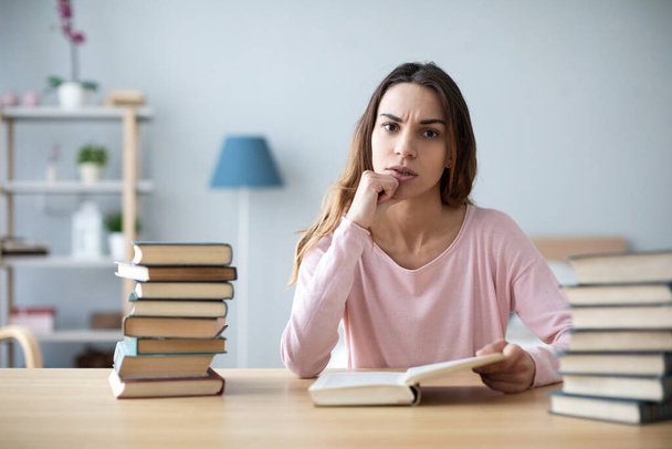 Female student sits at a table with books preparing for exams. Education, home studying concept. - Foto, Bild