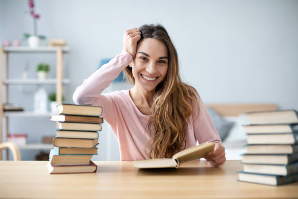 Portrait of young happy woman sits at a table with books studying at home. Education. - Фото, изображение
