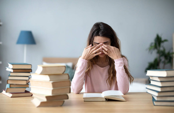 Upset young woman with books sit at work desk. Home studying concept. - Foto, afbeelding