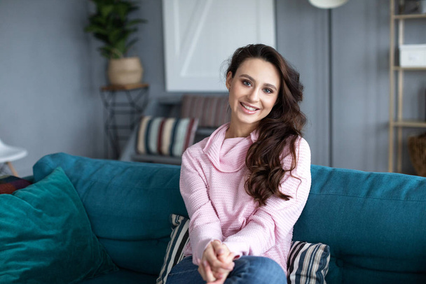 Beautiful smiling woman on sofa in living room. Portrait of a girl staying at home. - Foto, Imagem