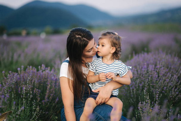 Portret atrakcyjnej młodej mamy z córeczką na lawendowym letnim polu. Szczęśliwa rodzina w dżinsowym stylu - Zdjęcie, obraz