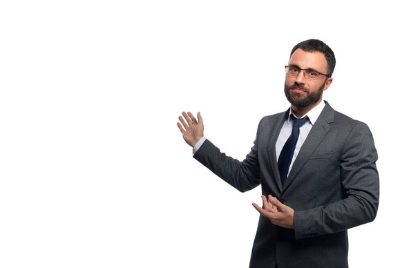 Homme d'affaires à lunettes avec une barbe regarde l'appareil photo pointant les mains sur le côté, une photographie de la taille - Photo, image