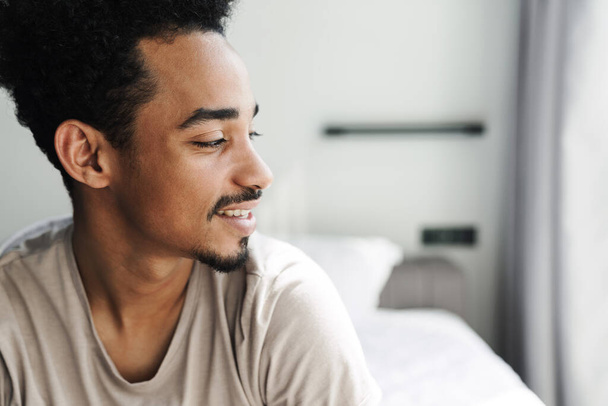 Photo of happy african american man with beard smiling after sleep in bed at bright room - Valokuva, kuva
