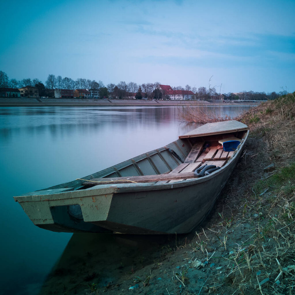 Un viejo barco de pesca usado varado en la orilla fangosa del río Sava al atardecer con nubes en el cielo. Transporte de agua en Bosanski Brod, Bosnia y Herzegovina. Bosanski Brod, Bosnia y Herzegovina
. - Foto, imagen