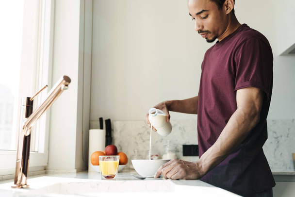 Photo of focused african american man with beard preparing breakfast in kitchen at home - Zdjęcie, obraz