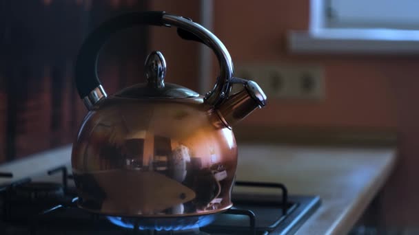 Egy rozsdamentes acél teáskanna bezárása egy lángoló gáztűzhelyen. Fogantatás. Fűtés vízforraló a reflexió a konyha a fém felületén, előkészítése forró ital. - Felvétel, videó