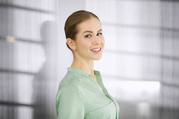 Beautiful adult business woman dressed in green blouse standing straight in office. Business headshot or portrait - Foto, Imagen
