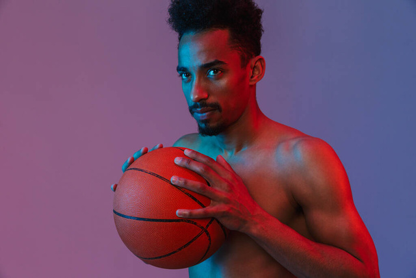 Portrait of sporting shirtless african american man poising with basketball isolated over violet background - Φωτογραφία, εικόνα