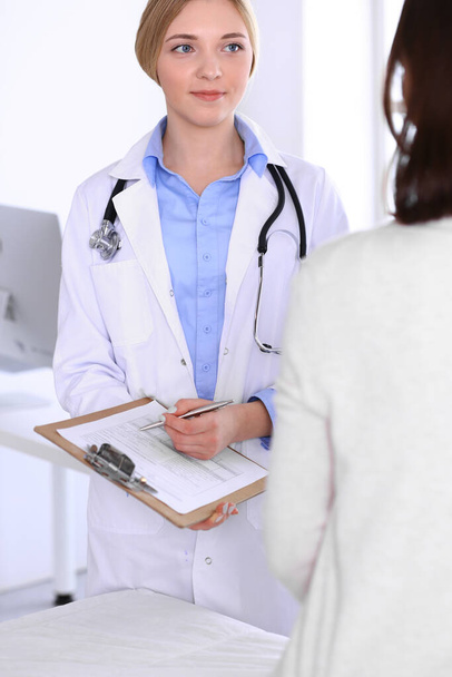 Young woman doctor and patient at medical examination at hospital office. Blue color blouse of therapist looks good. Medicine and healthcare concept - Foto, Bild
