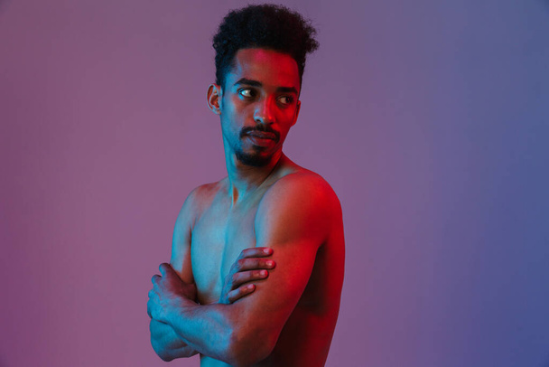 Portrait of young handsome shirtless african american man poising on camera with his arms crossed isolated over violet background - Fotó, kép