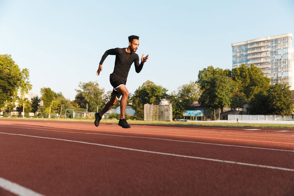 Image of strong african american man running on sports stadium outdoors - Фото, зображення