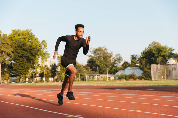 Image of athletic african american man running on sports stadium outdoors - Foto, imagen