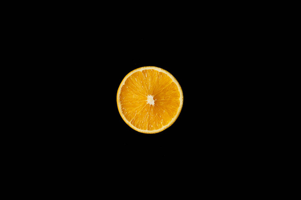 Corte naranja por la mitad, una fuente de luz, primer plano sobre fondo negro
 - Foto, Imagen