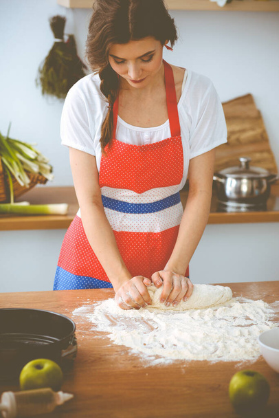 Young brunette woman cooking pizza or handmade pasta in the kitchen. Housewife preparing dough on wooden table. Dieting, food and health concept - Фото, зображення