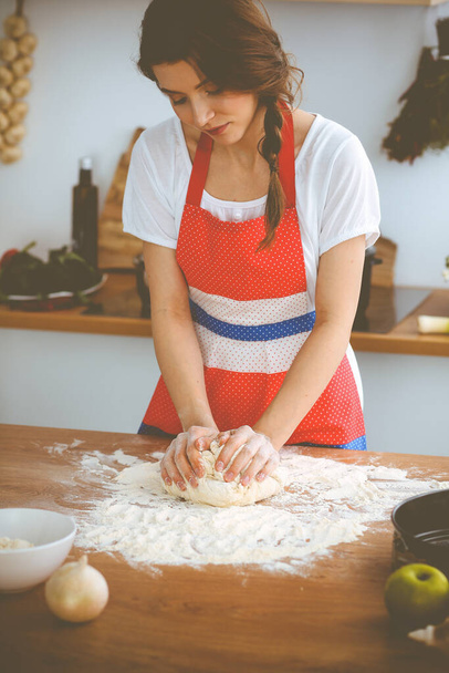 Young brunette woman cooking pizza or handmade pasta in the kitchen. Housewife preparing dough on wooden table. Dieting, food and health concept - 写真・画像