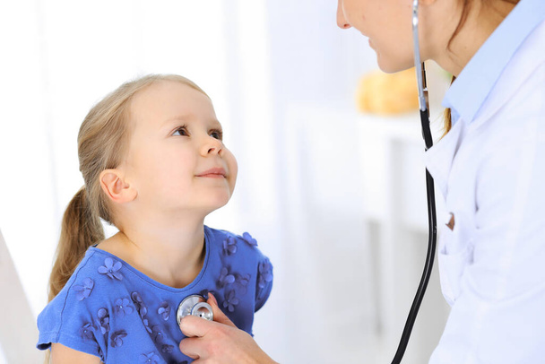 Doctor examining a little girl by stethoscope. Happy smiling child patient at usual medical inspection. Medicine and healthcare concepts - Photo, image