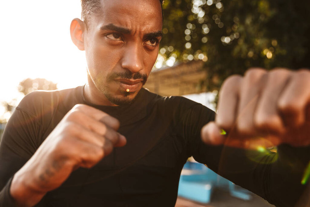 Image of muscular african american man clenching fists and boxing on sports ground outdoors - Foto, imagen