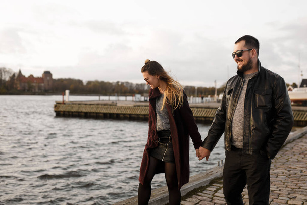 Beautiful good-looking couple in casual style hilding hands together walking on the waterfront. Urban style. Walking around the city. - Photo, Image
