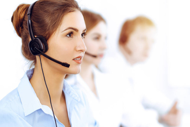 Call center operators. Focus on beautiful business woman using headset in sunny office - Foto, Imagen